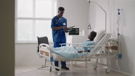 african-american-woman-resting-in-hospital-bed-after-surgery-talking-to-young-male-nurse.-Portrait-of-african-american-nurse-assisting-ill-female-patient-lying-in-bed