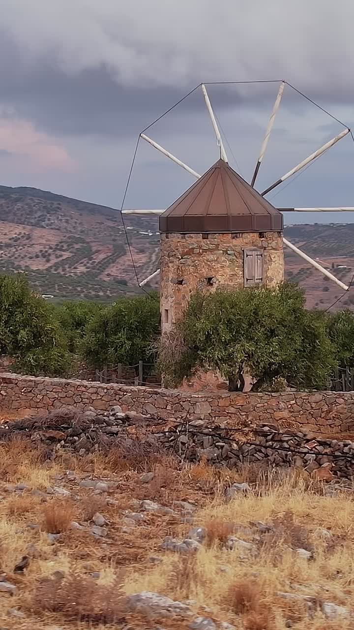Mulino a vento tradizionale in pietra in un paesaggio collinare arido con cielo nuvoloso