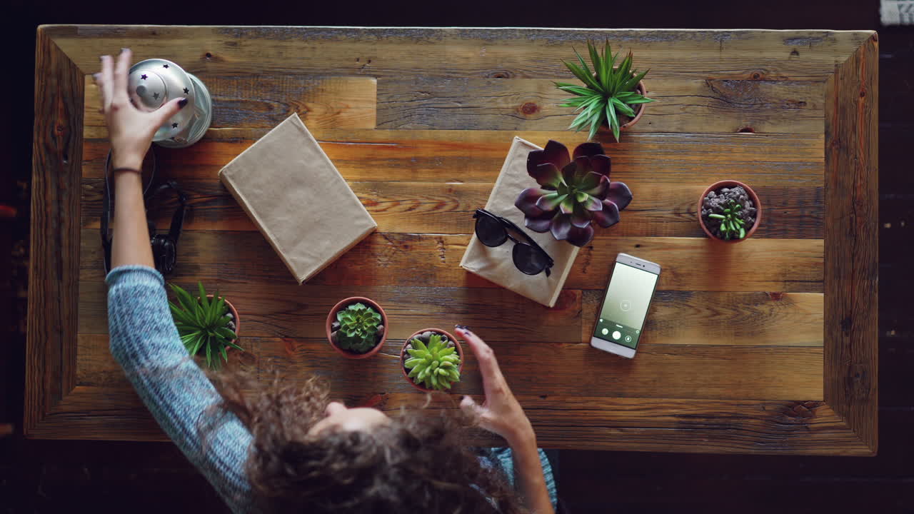 Woman Taking a Photo of Succulents and Gifts on a Wooden Table