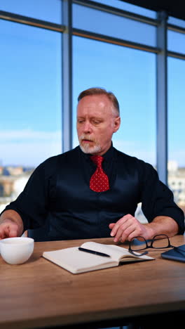 hard-working male in the modern office. tired employee takes off his glasses and drinks from the cup. vertical video.
