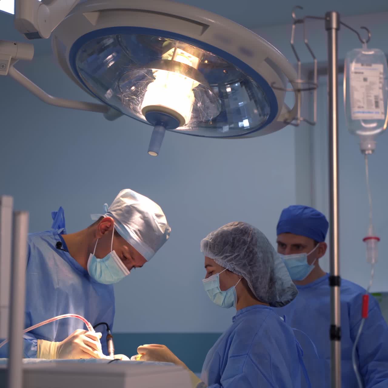 Chief surgeon works with two tools at once holding them with both hands. Female assistant uses syringe to emit the liquid on the surgery locality
