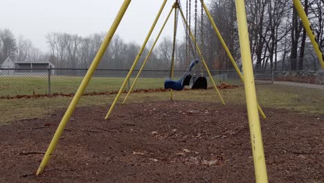 deserted playground swings through the frame swinging empty and lonely on a rainy and dreary day