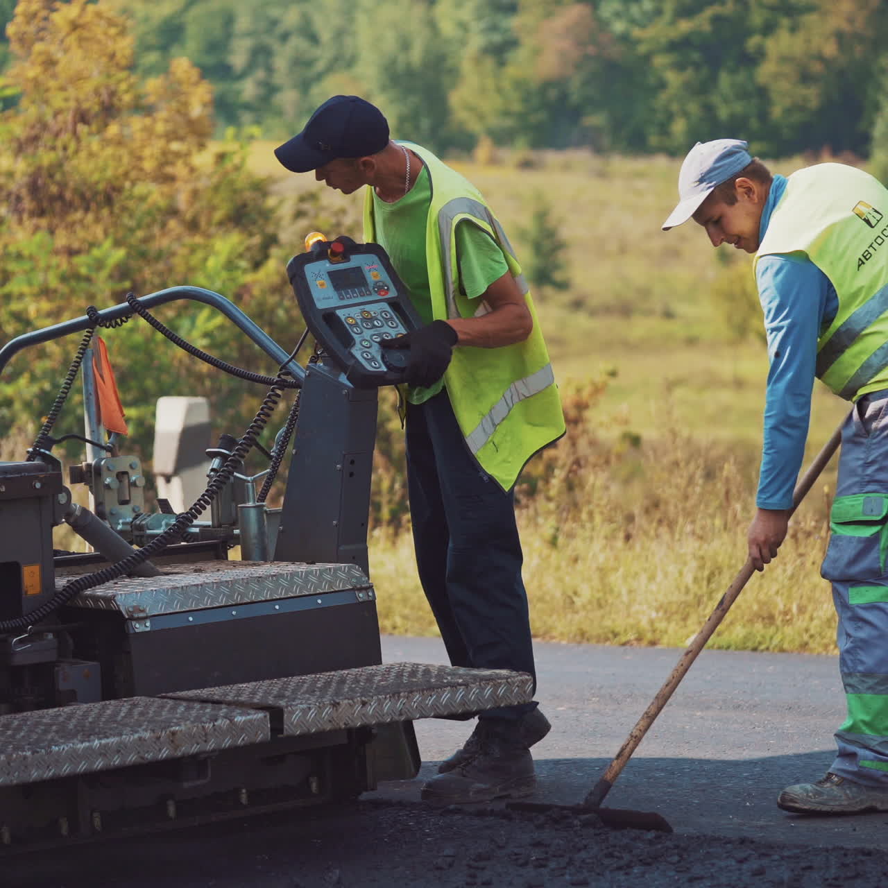 Workers during road asphalting outdoors. Fresh asphalt resurfacing on the road and workers are leveling up hot bitumen with special instrument.