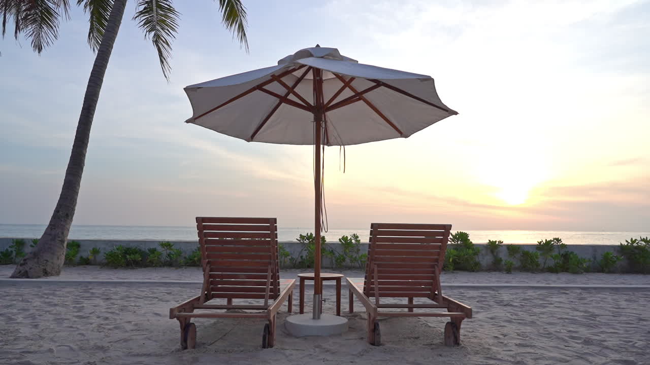 con la puesta de sol a lo lejos, un par de tumbonas vacías se sientan bajo una sombrilla en la playa