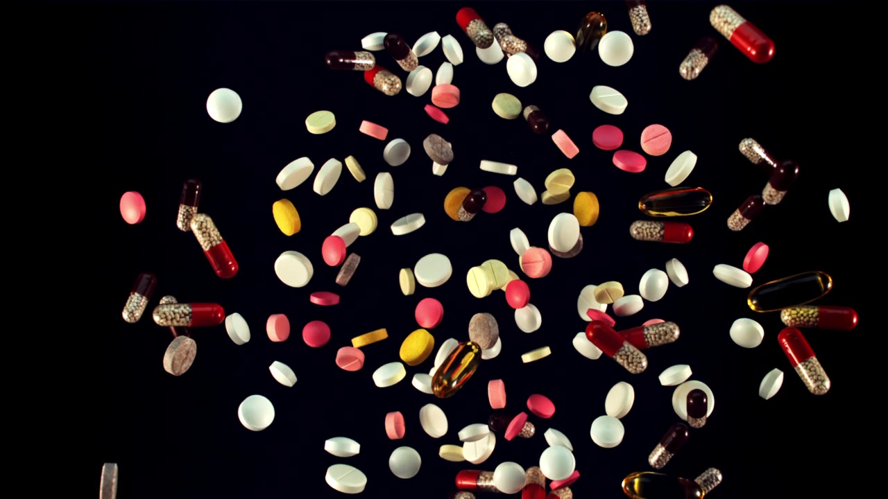 Various Pills and Capsules Falling in Slow Motion on Black