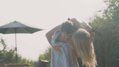 mother wrapping young son in towel by outdoor swimming pool on summer vacation