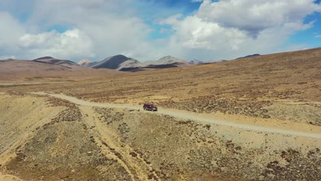 Aerial-drone-of-a-red-suv-driving-along-a-dirt-road-path-in-the-high-altitude-alpine-orange-plain-of-Deosai-National-Park-located-between-Skardu-and-Astore-Valley-in-Pakistan-on-a-sunny-summer-day