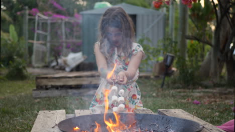 young girl roasting marshmallows on metal sticks over backyard fire