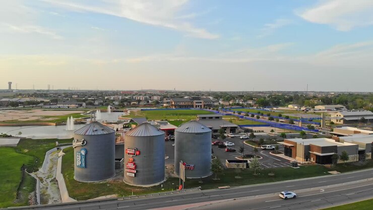 Muovendosi rapidamente ad arco verso sinistra per mostrare lo sviluppo del centro città che presenta 3 iconici silos per gin come parte di un progetto di sviluppo urbano