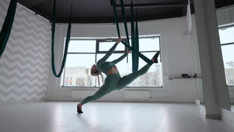 young beautiful woman practice in aero stretching swing. young woman rolls her head upside down in a hammock for aerial yoga. focused pretty mature woman doing aerial yoga in gym