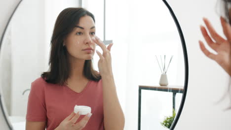 Woman applying face cream in front of a mirror