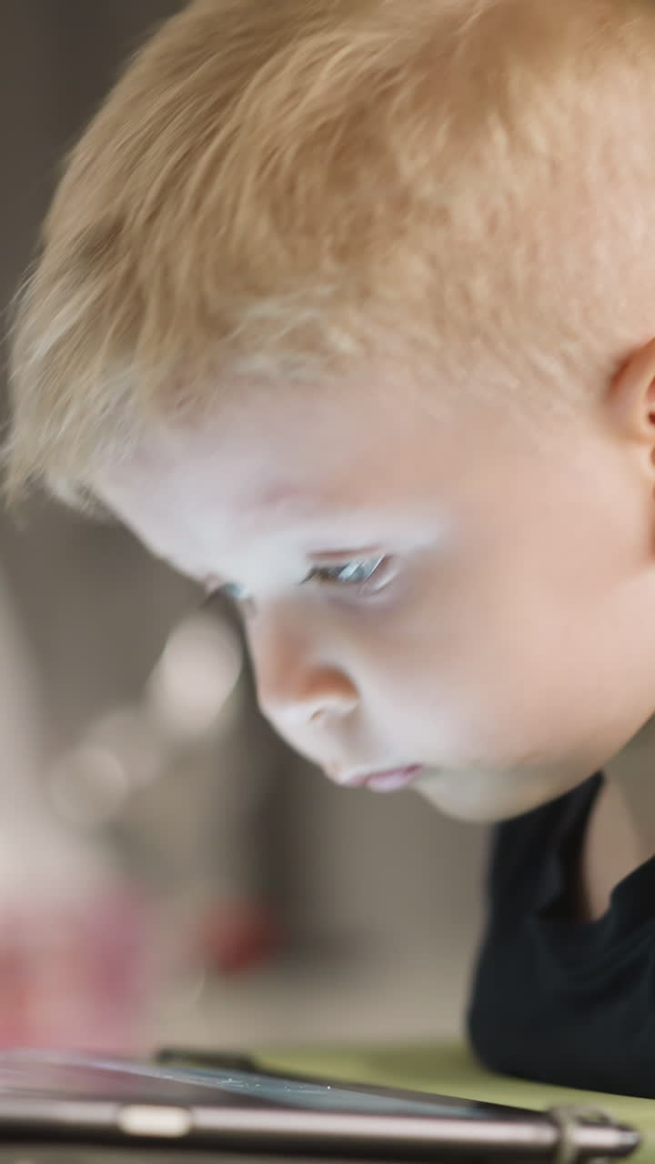 Cute little boy nods head watching education lesson via tablet computer at home closeup. Toddler kid tired of fun with digital gadget. Electronic device