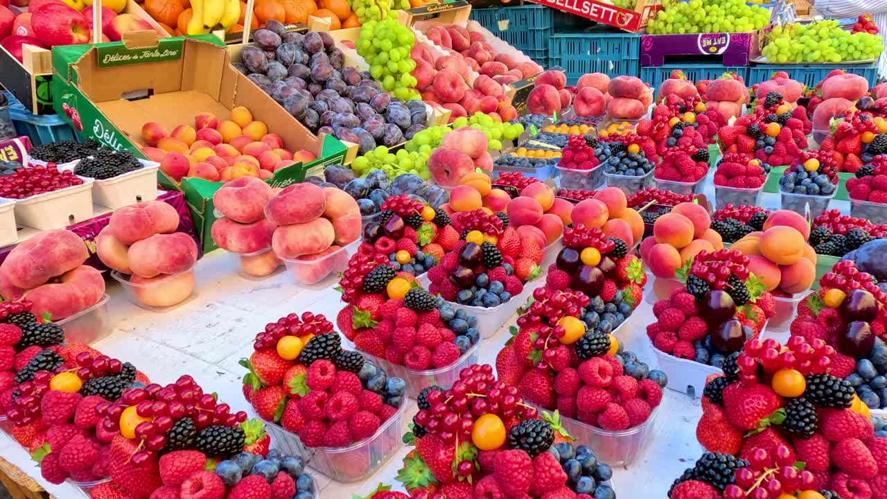 Colorful baskets of peaches, raspberries, blackberries, and currants displayed on a market stall in natural daylight, with slow camera pan