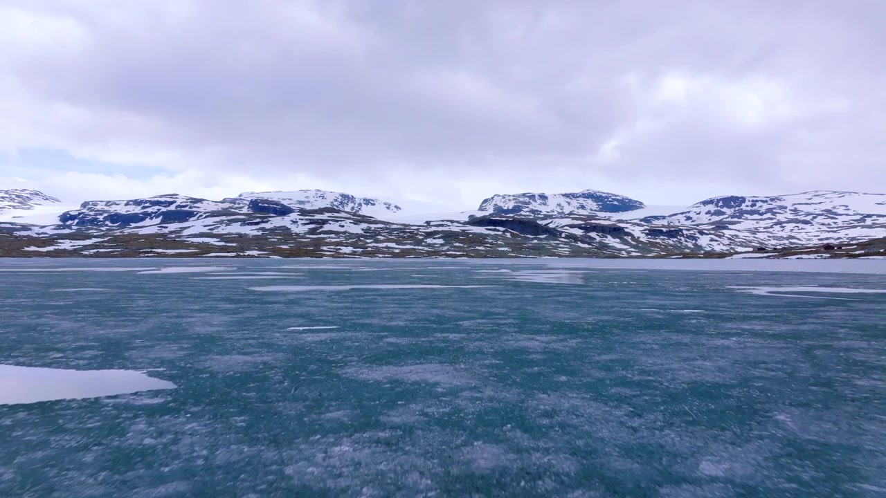 Droneflyvning over smeltende is på Finsevatnet, der viser den sæsonmæssige overgang i skyggen af Hardangerjøkulen gletsjeren.