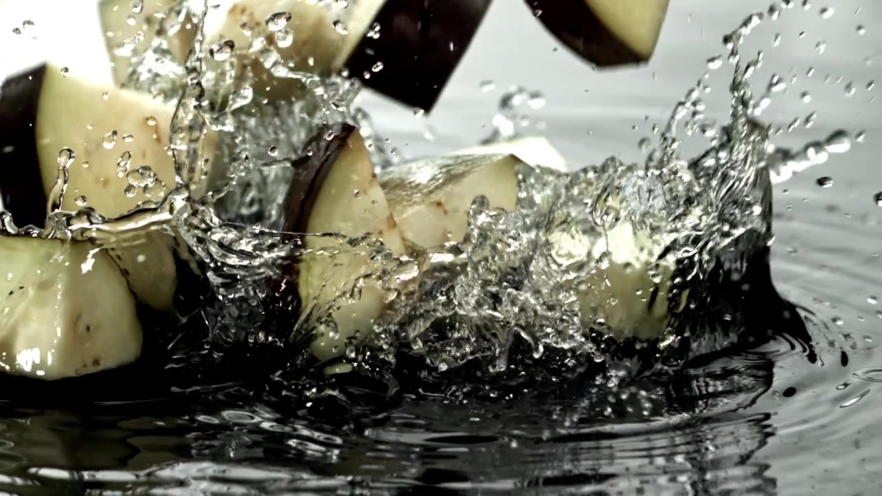 Pezzi di melanzana tritati che schizzano nell'acqua al rallentatore