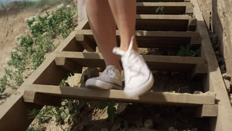 slim girl legs running down beach staircase wearing white sneakers close up.