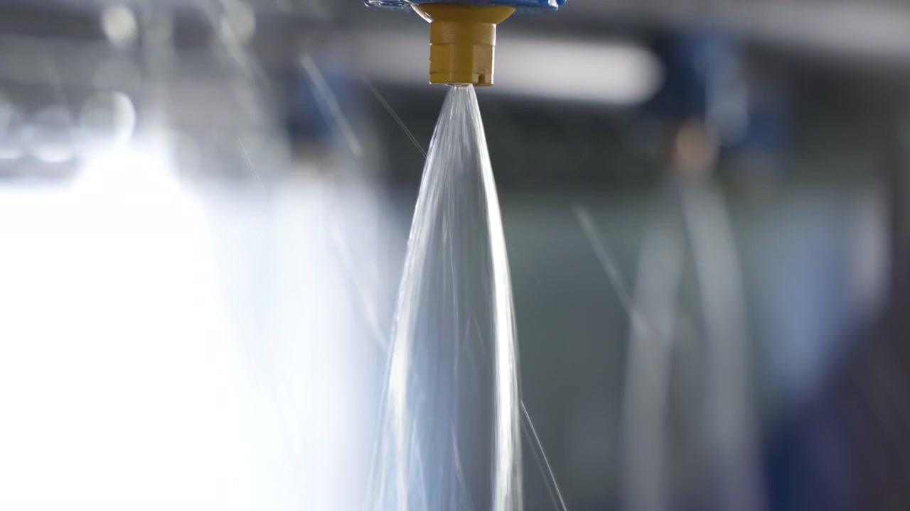 Getti d'acqua ad alta pressione fuoriescono da ugelli di nebulizzazione industriali all'interno di una stazione di lavaggio di un impianto di lavorazione HPP per avocado