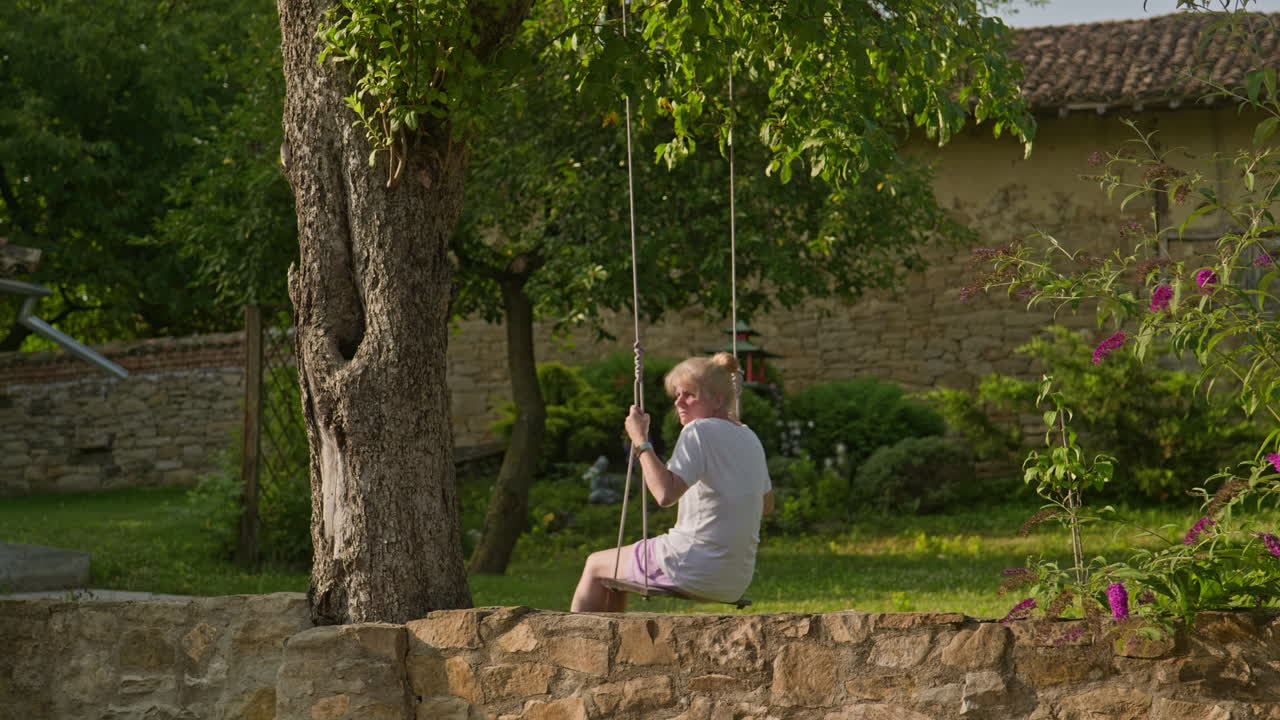 Donna su un'altalena su un melo si gode la pace e la solitudine del suo bellissimo giardino.
