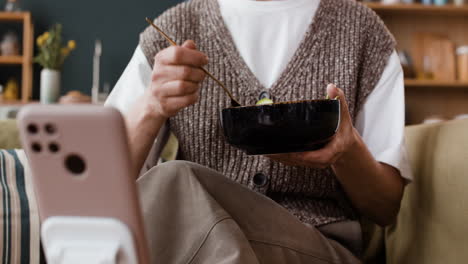 person eating while watching smartphone on a stand