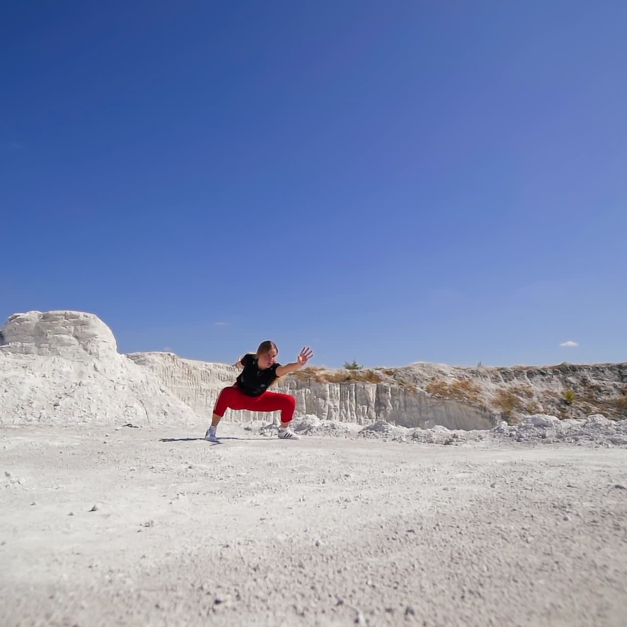 Chubby blonde girl performing a tumble. Dancer showing the acrobatic move on the white rocky landscape. Blue sky backdrop