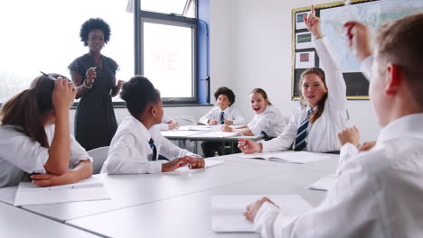 Tutora-De-Secundaria-Preguntando-A-Los-Alumnos-Uniformados-Sentados-En-Los-Escritorios-Una-Pregunta-A-La-Que-Levantan-La-Mano