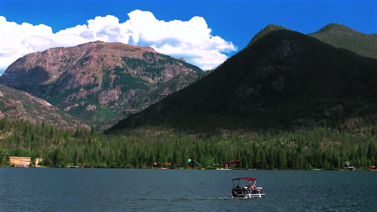 Grand Lake Granby pontoon boating sailboat spring summer aerial drone Colorado Rocky Mountains National Park entrance sunny morning daytime clouds lake homes blue sky sunny clouds pan left motion
