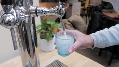 Hombre-Vertiendo-Agua-Gaseosa-De-Un-Grifo-Moderno-En-Un-Vaso-Azul