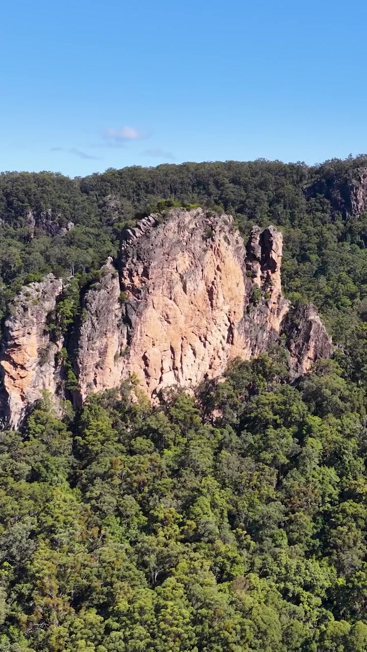 Riprese con drone che catturano imponenti formazioni rocciose vulcaniche circondate da una fitta foresta verde sotto cieli azzurri.