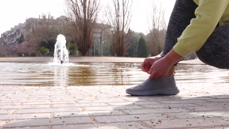 sporty woman tying her sneakers in park with a nice fountain in the background