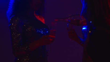 close up of two women in nightclub bar or disco pouring drinks from bottle 1