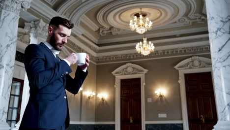 man in a suit drinking coffee in an elegant, ornate lobby
