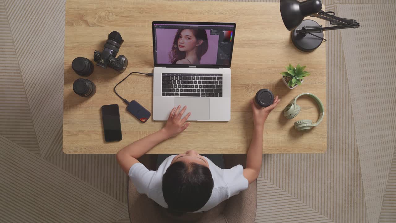 Top View Of Asian Woman Editor Drinking Coffee While Sitting In The Workspace Using A Laptop Next To The Camera Editing Photo Of A Woman At Home