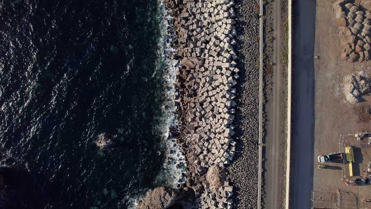 Onde atlantiche che si infrangono su un frangiflutti di cemento accanto alla strada costiera al Miradouro da Costa Norte, Parco Naturale della Costa Vicentina, Sines, Distretto di Setúbal, Alentejo, Portogallo — ripresa aerea dall'alto con drone