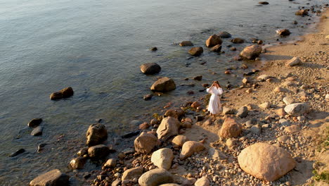 woman spins twirling hair dress walking along rocky boulder beach