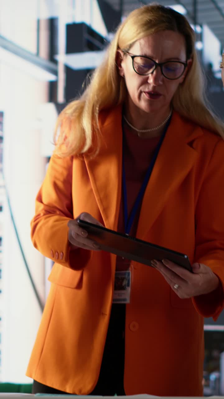 Forretningskvinde i orange blazer, der diskuterer projekt på tablet med kolleger.
