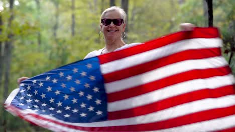 blonde woman spinning to the left holding an american flag in a forest with shallow depth of field