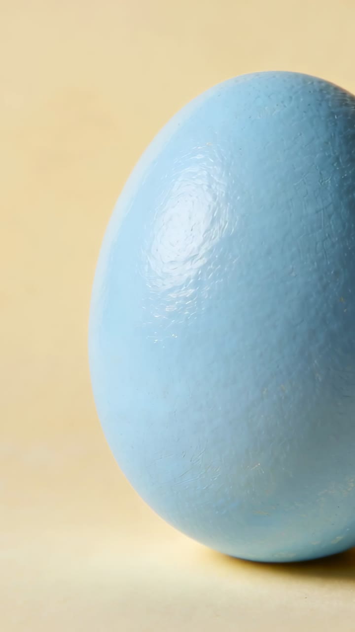 Vertical video: Panning camera revealing pale-blue egg sliding left on yellow backdrop tabletop