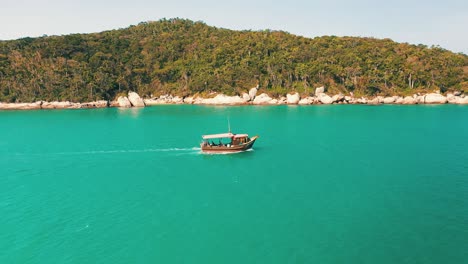 Side-aerial-view-of-a-tourist-boat-passing-by-on-turquoise-water-color-and-paradisiac-tropical-rainforest-scenery-with-a-bunch-of-seagulls-flying-by