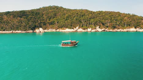 side aerial view of a tourist boat passing by on turquoise water color and paradisiac tropical rainforest scenery with a bunch of seagulls flying by