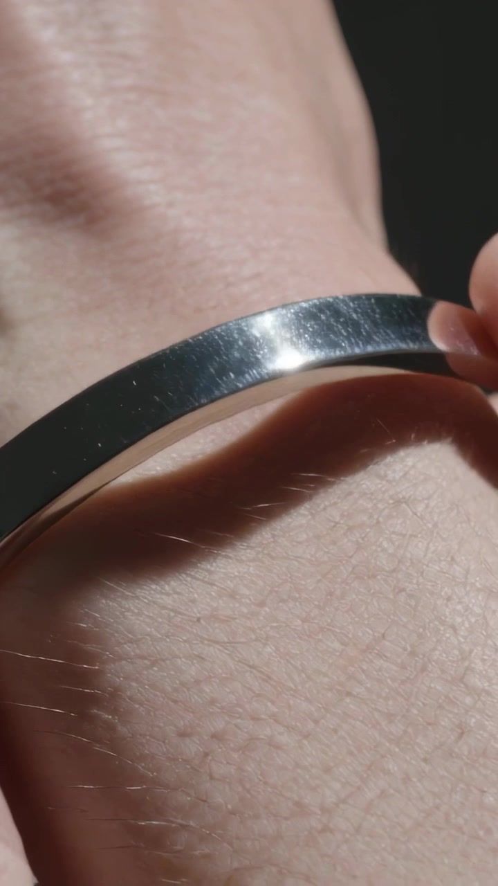 Vertical video: Sliding fingertips holding metal bangle onto wrist in close-up, securing fit