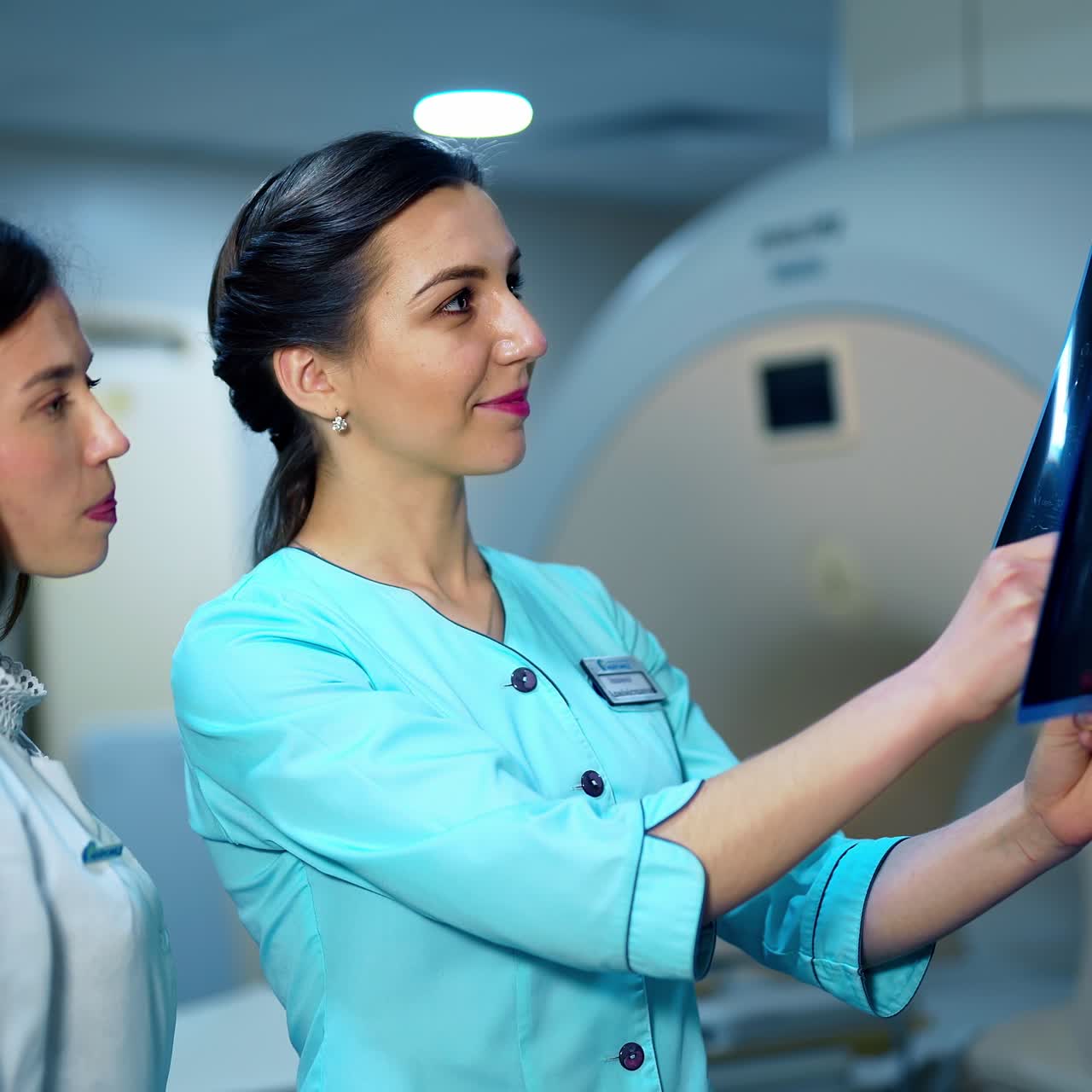 Female doctors analyzing x-ray together. Young women in medical uniform examining x-ray photo of a patient on the background of modern equipment in clinic.