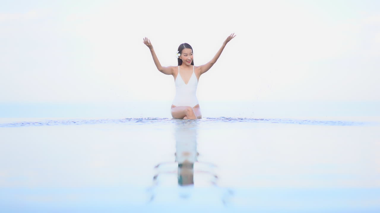 인피니티 풀에서 날씬한 아시아 여성 재생 및 물 분사, 슬로우 모션