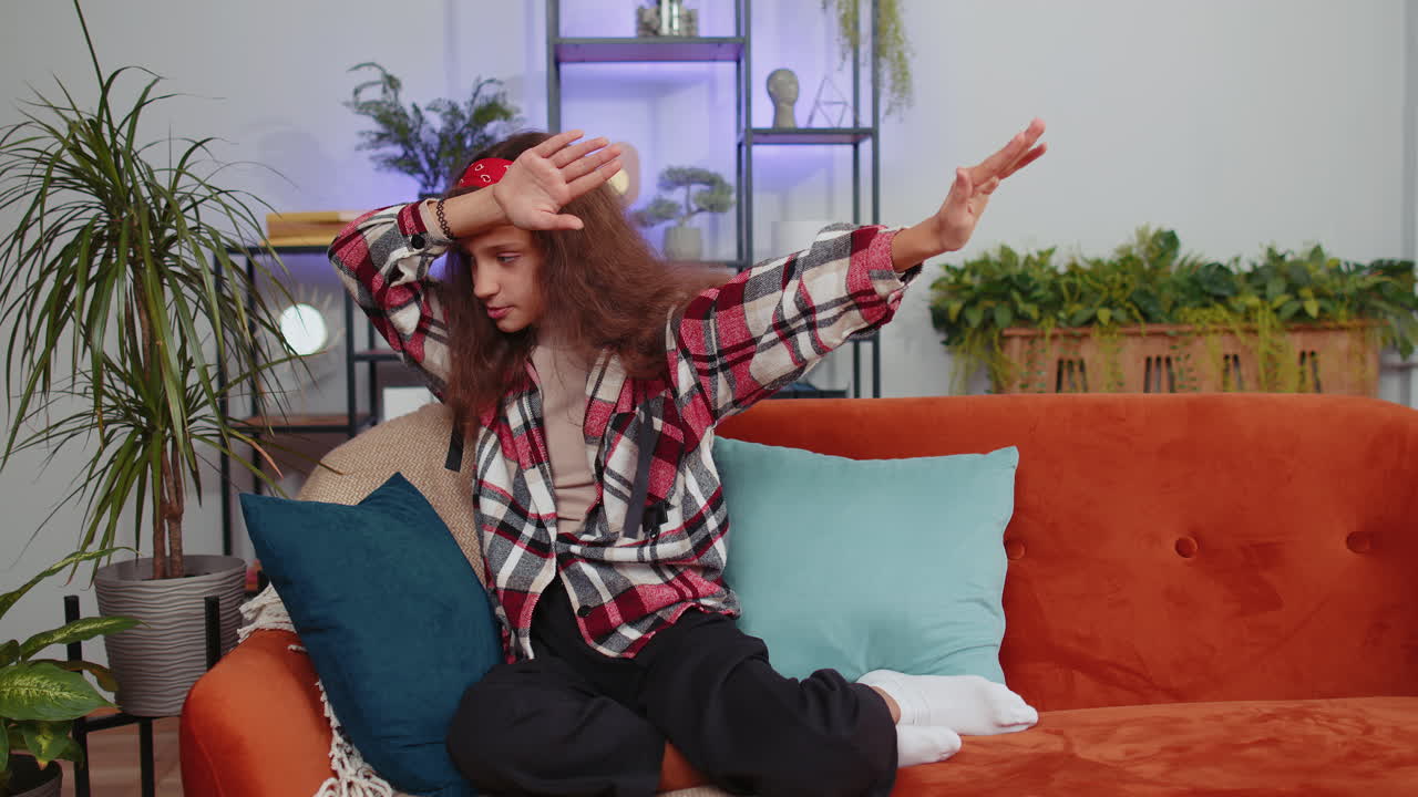 트렌디하고 즐거운 긍정적인 소녀가 춤을 추고 리 ⁇ 에 따라 움직여 현대 가정에서  ⁇  댄스 제스처를 만 ⁇ 니다.