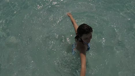 top, areal view of a young girl in swimwear having fun and making circles on a beach with crystal clear water around her