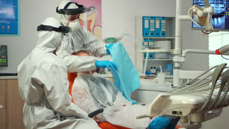 man assistant in protective suit putting dental bib to kid