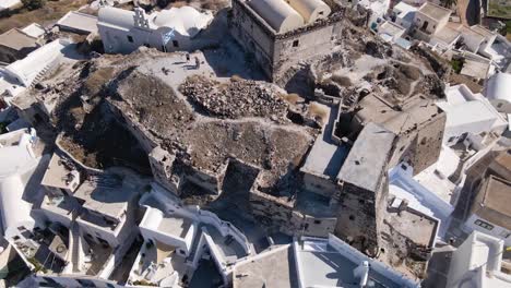 Vista-Aérea-De-Arriba-Hacia-Abajo-Del-Castillo-Veneciano-Que-Se-Inclina-Sobre-El-Pueblo-De-Akrotiri-En-Santorini,-Grecia