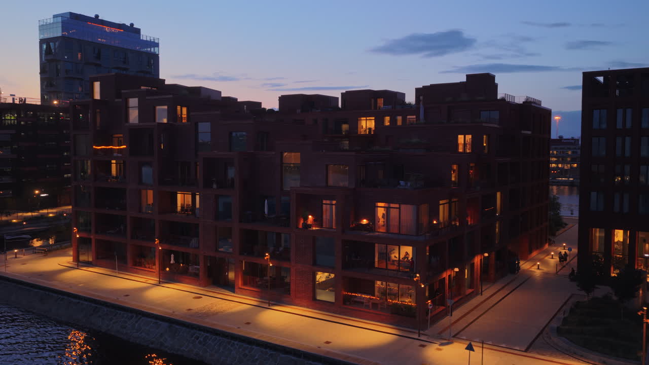 Aerial drone view of modern apartments along the waterfront promenade in Copenhagen, Denmark, with warm lights reflecting on the water