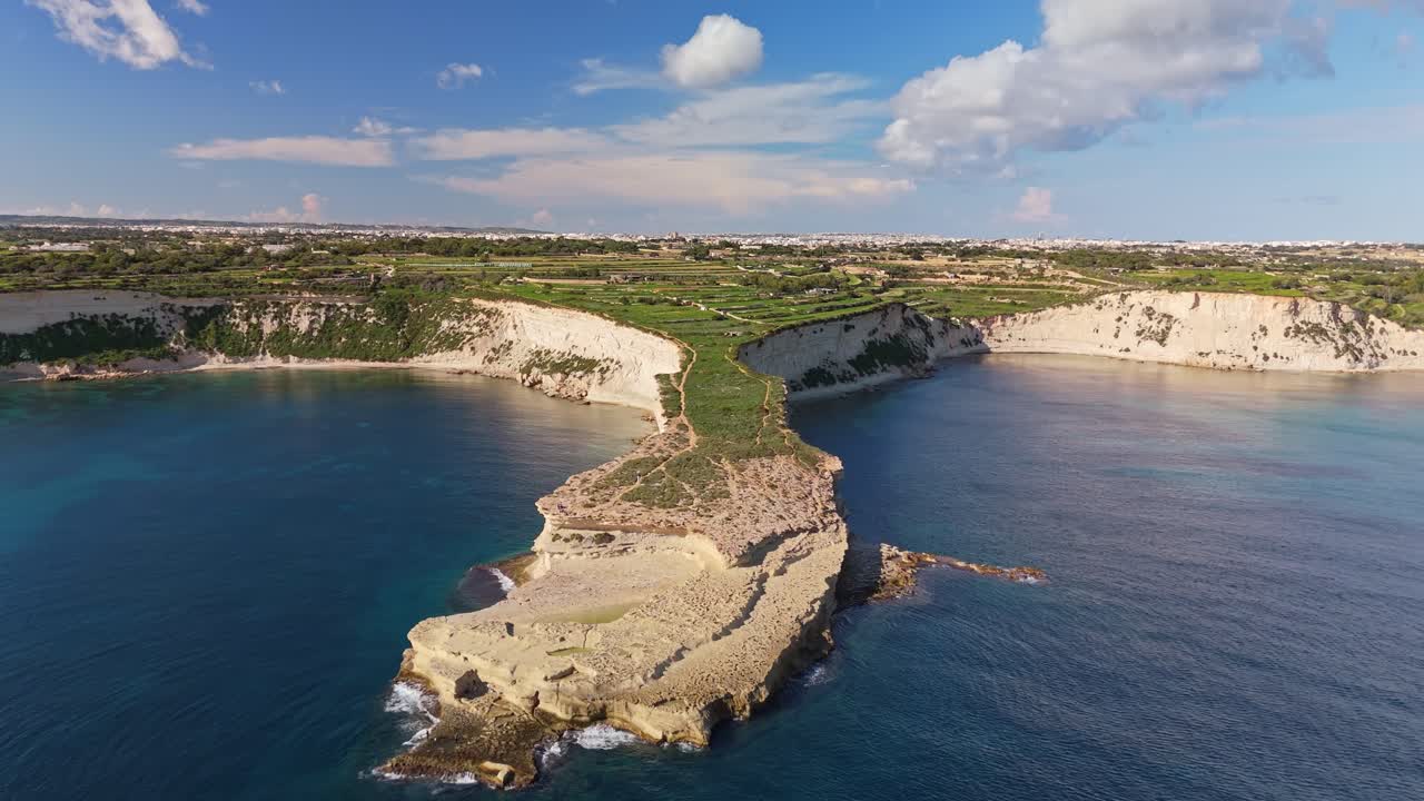 Drone som flyr mot en steinete maltesisk halvøy om vinteren og avslører nydelige kalksteinsklipper, krystallklart middelhavsvann og et fredelig kystlandskap under en klar, blå himmel