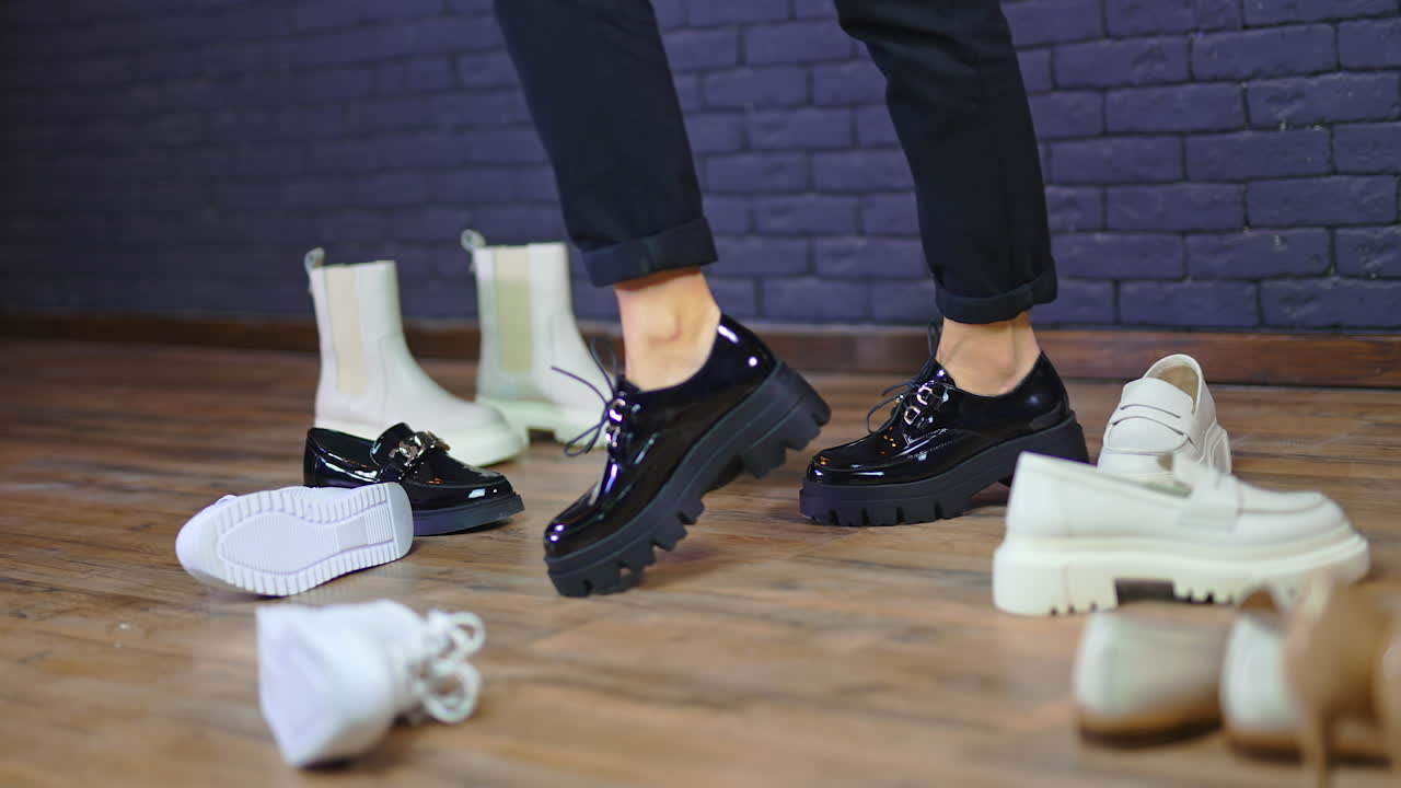 Woman is twisting and turning, showing the black lacquer shoes with laces. Model demonstration among other footwear. Blue wall backdrop.