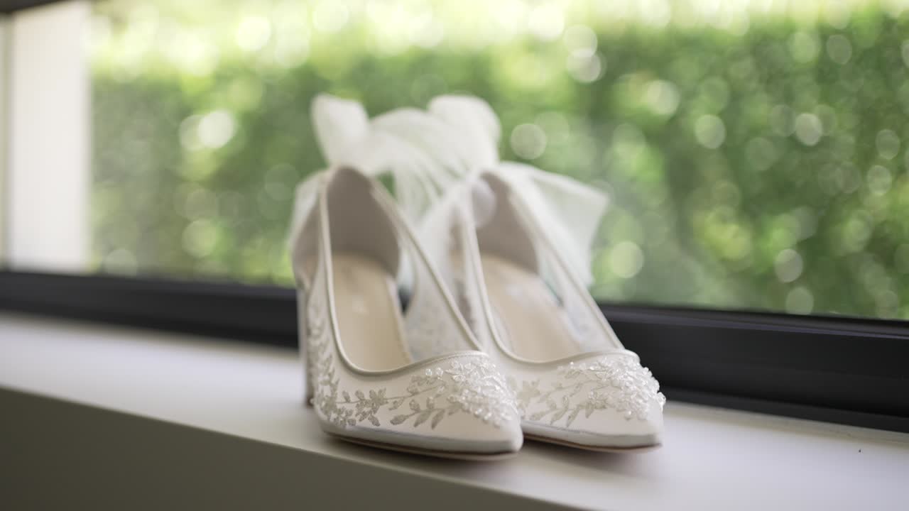 White bridal shoes with delicate lace details displayed on a windowsill in soft light